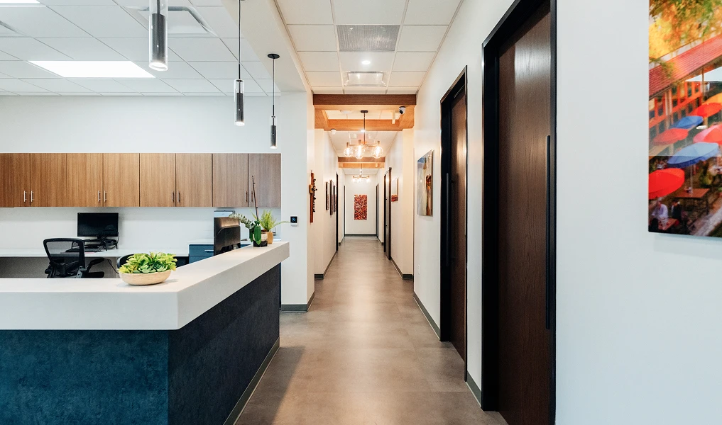 Modern office kitchen with white countertops, dark cabinets, and hallway leading to conference rooms