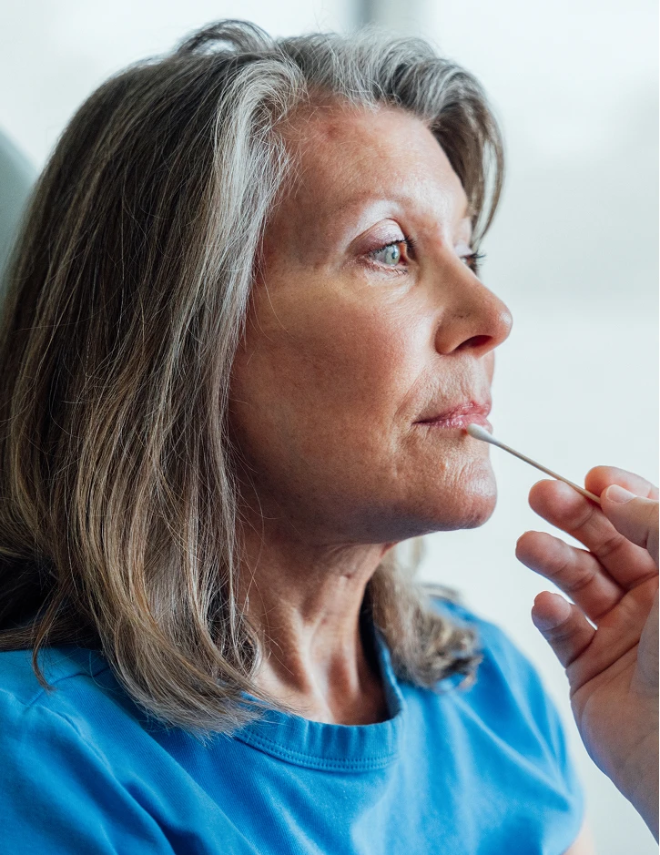 Mature woman with gray hair in blue shirt applying lipstick in natural light, side profile view