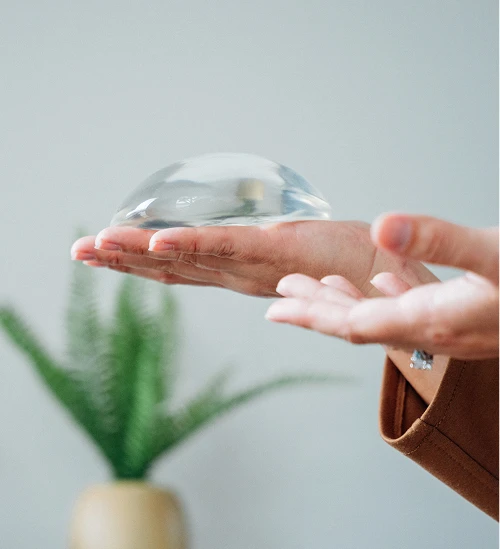 Hand holding implant in palm with plant in background - Breast augmentation in San Antonio, TX