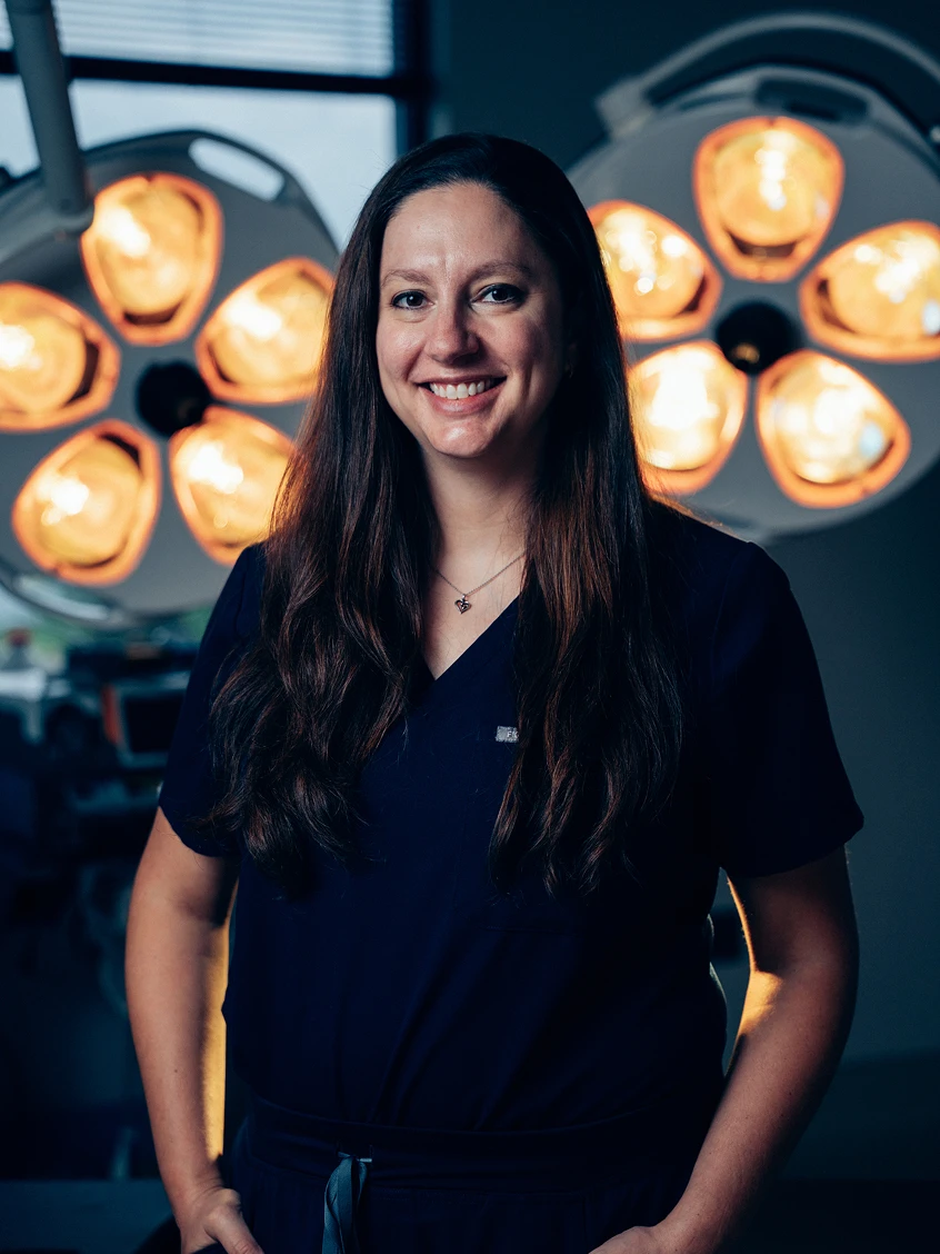 Dr Rokosz in scrubs smiling in front of surgical lights in operating room - Doctor in San Antonio, TX