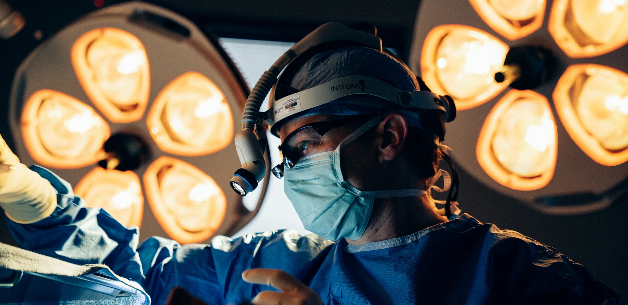 Dr Rokosz performing operation under bright surgical lights in operating room wearing mask and scrubs - Doctor in San Antonio, TX