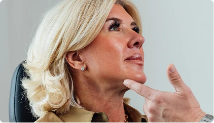 Blonde woman looking upward with hand gesture, professional headshot with light background - Facelift in San Antonio, TX