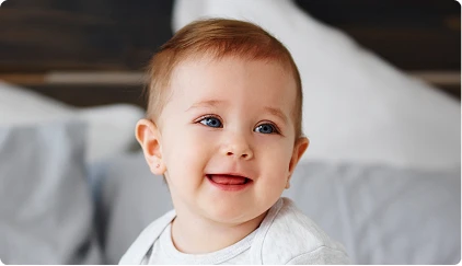 Happy red-haired toddler smiling at camera while sitting on white bed - lip in San Antonio, TX