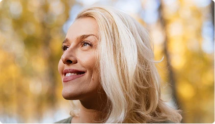 Woman with blonde hair smiling outdoors in autumn sunlight with golden foliage background - Trauma in San Antonio, TX