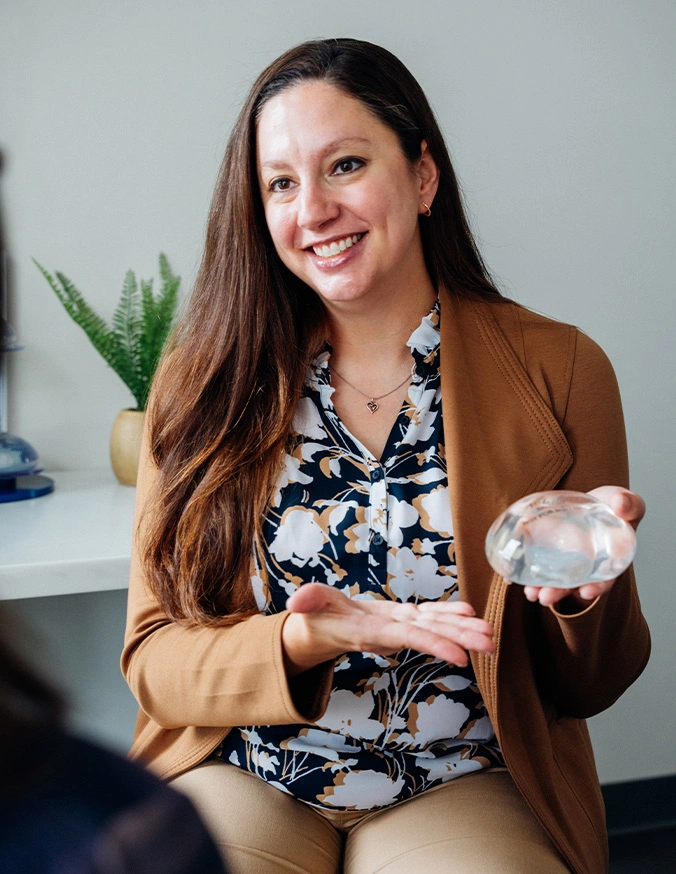 Professional woman in tan blazer presenting breast implant while smiling at camera - Breast augmentation in San Antonio, TX