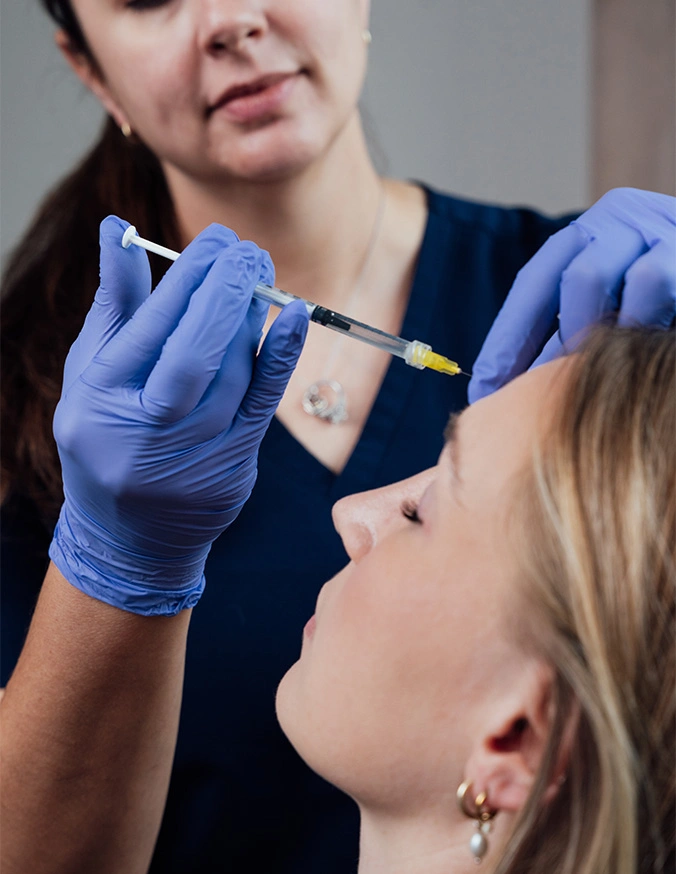 Healthcare professional injecting filler into patients forehead using medical instrument while wearing blue gloves - Botox in San Antonio, TX