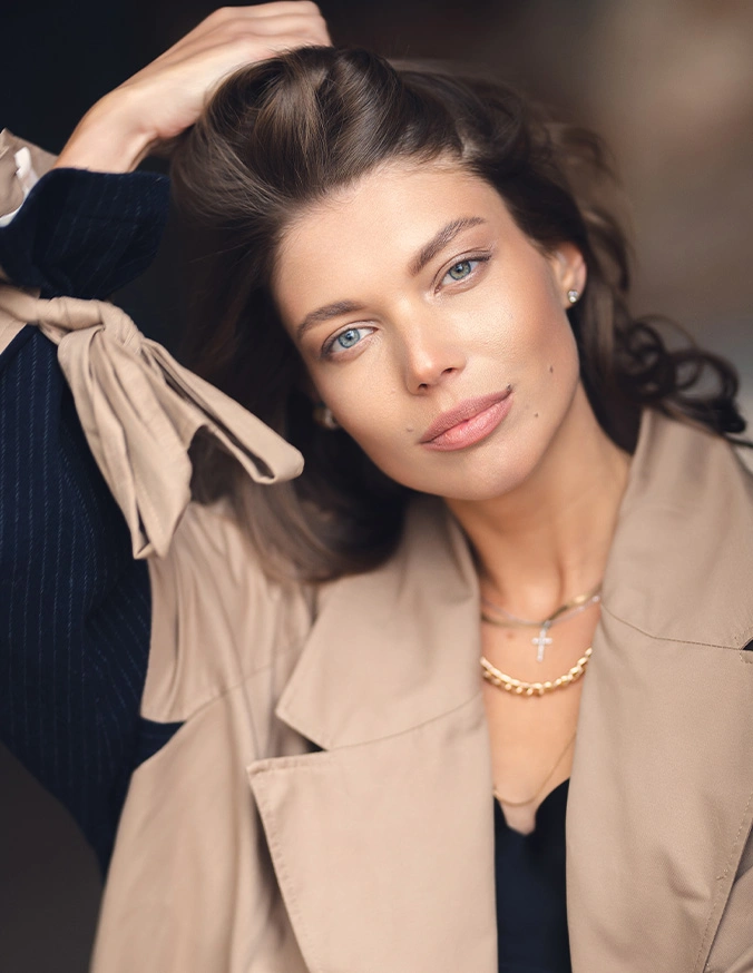 Professional woman in beige blazer and pearl necklace posing with hand in dark hair against blurred background - Brow lift in San Antonio, TX