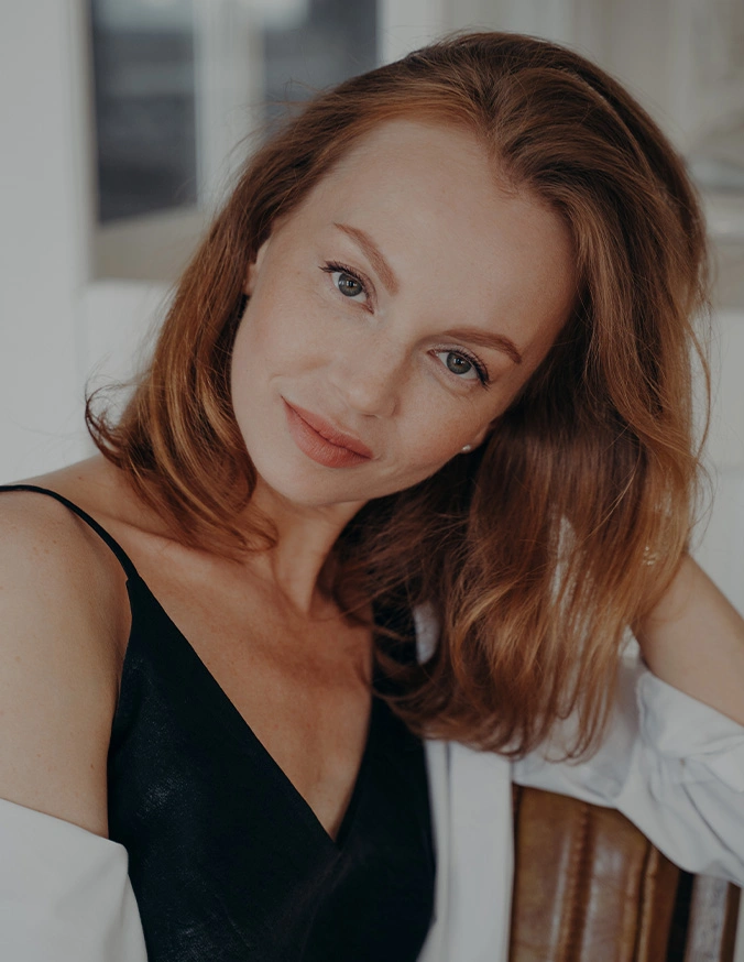 Young woman with wavy auburn hair in black dress posing indoors with natural lighting - Chemical peels in San Antonio, TX