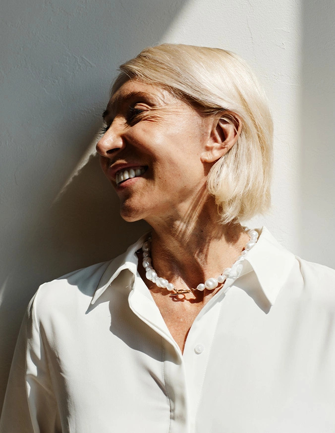 Smiling woman with platinum blonde hair wearing white shirt and beaded necklace in natural light - Earlobe repair in San Antonio, TX