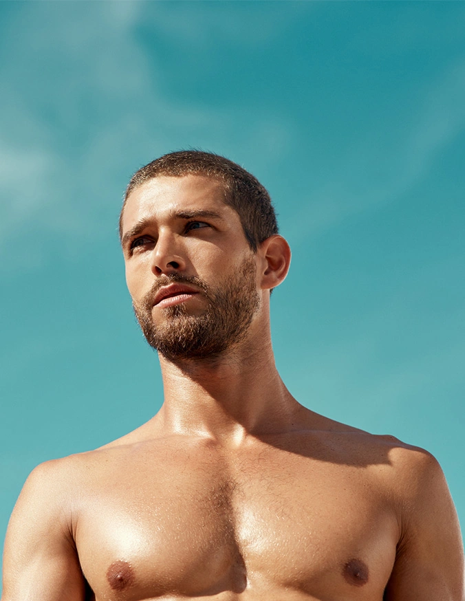 Shirtless bearded man looking up against clear blue sky in natural sunlight - Gynecomastia in San Antonio, TX