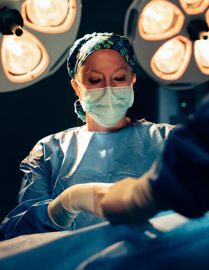 Dr Rokosz in surgical mask and gown performing operation under bright operating room lights - Liposuction in San Antonio, TX