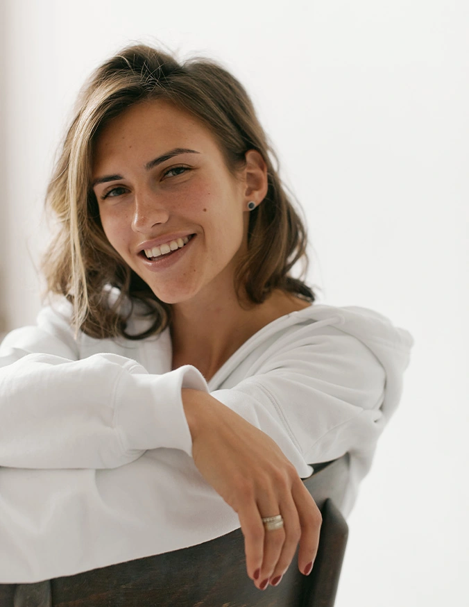 Young woman in white shirt smiling at camera with arms crossed in bright natural light - Liquid rhinoplasty in San Antonio, TX