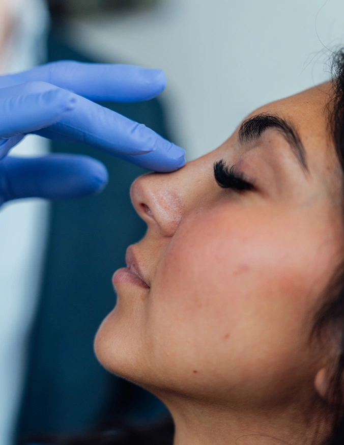 Woman receiving facial cosmetic injection treatment from medical professional wearing blue gloves - Nasal fracture surgery in San Antonio, TX