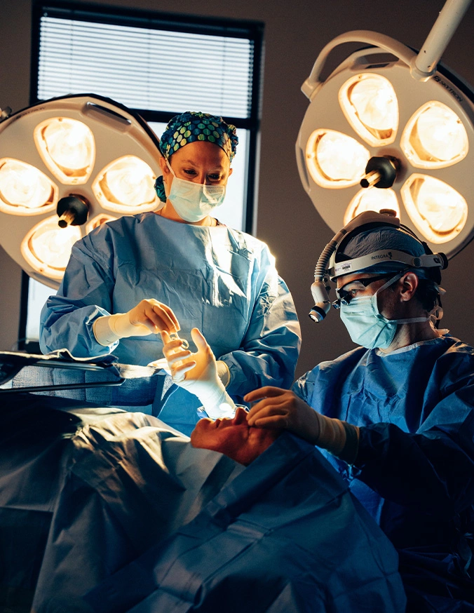 Dr Stallworth MD and Dr Rokosz performing operation in modern operating room with overhead lights and medical equipment - Revision rhinoplasty in San Antonio, TX