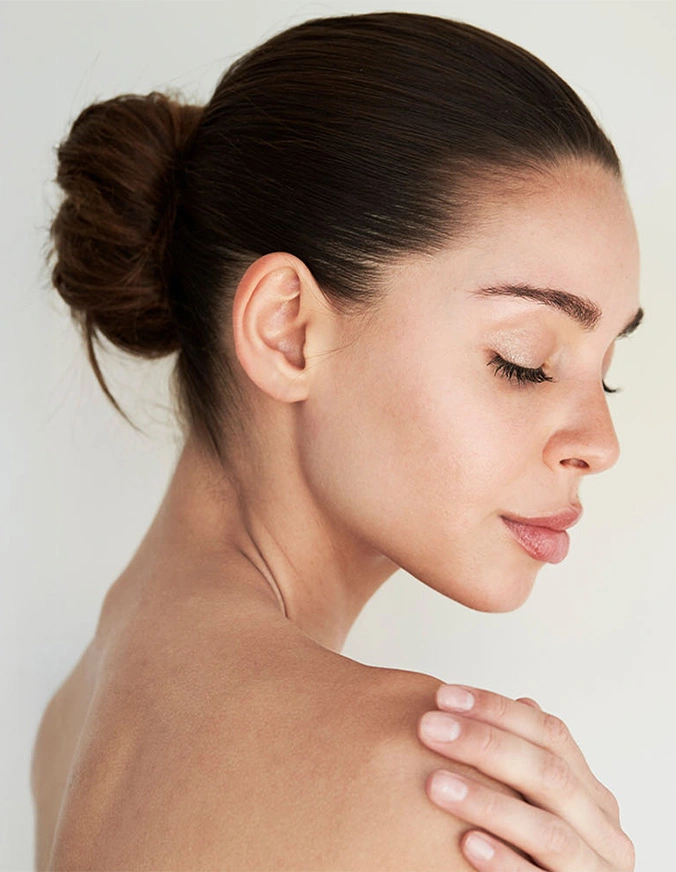Woman with clear skin and hair in bun touching shoulder showing skincare and beauty routine results - Scar revision in San Antonio, TX