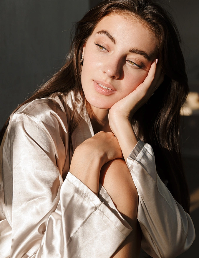 Young woman in white shirt posing with hand on face in natural sunlight, soft portrait photography - Skincare in San Antonio, TX
