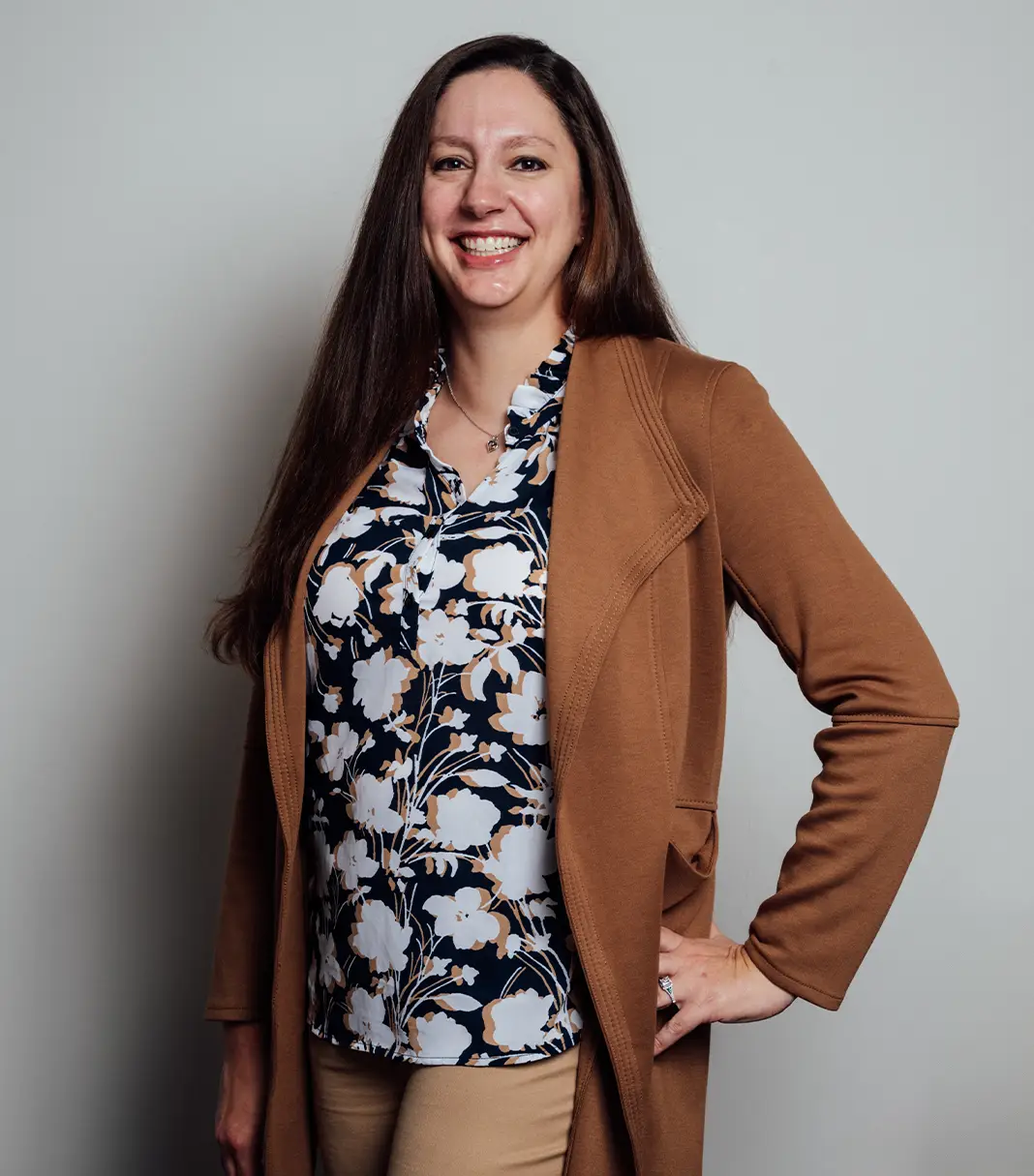 Dr Rokosz with long dark hair in tan blazer and floral top smiling at camera against white background - Doctor in San Antonio, TX