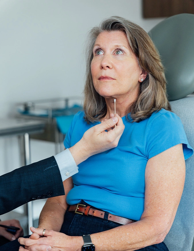 Doctor examining mature woman's thyroid gland during medical consultation in clinical setting - Necklift in San Antonio, TX